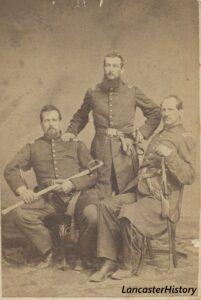 Three men in Civil War era uniforms; man in center is standing
