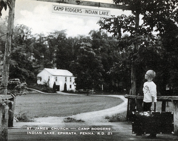 An unidentified camper lugs his foot locker through the gates of Saint James’ Camp Rodgers at Indian Lake in Clay Township, Lancaster County, c. 1960.