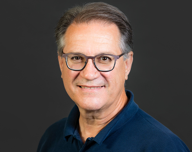 Headshot image of Patrick Clarke, an older light skinned man wearing a dark blue polo shirt and brownish glasses.