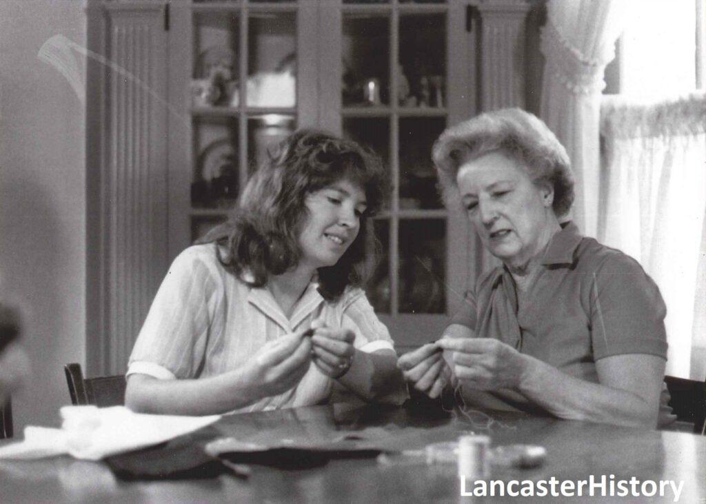 Two women sitting at a table working on a quilt. 