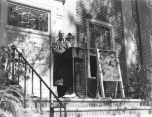 Man standing at podium with bronze plaque to his left side.