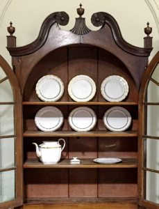 China cupboard showing seven plates and one teapot; white glaze with gold trim.