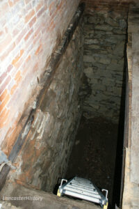 Interior view of the icehouse featuring a 12 foot deep pit with stone walls and a dirt floor