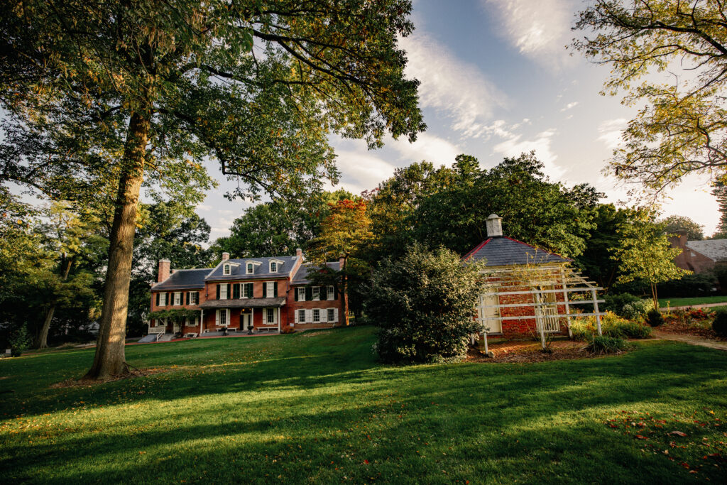 A view of two brick buildings with an expansive green grass and tall trees around them.