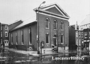 Brick church building, four long windows on one side. Three windows across front on second floor. Two windows with door in center on first floor