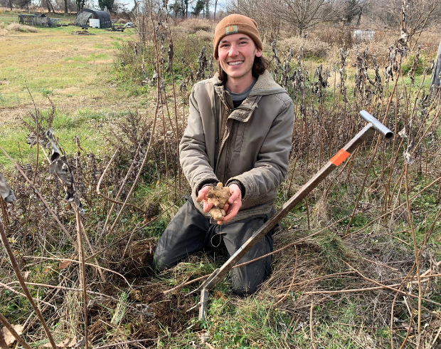A young man wearing a thick outdoor jacket presents a sunchoke tuber.