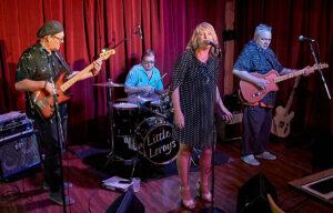 Two men on guitars, a man on drums, and a woman singing.