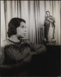 Black and white image of a dark-skinned woman with dark hair dressed in gown with black embroidery on the front.