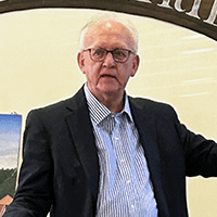 Image of Bruce Mowday, an older man with light skin wearing a suit jacket.