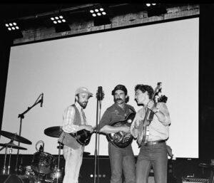 A black and white photo of three young men with various string guitar instruments.