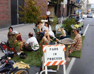Photo of a group of people sitting in a parking space that has been transformed into a mini green space.