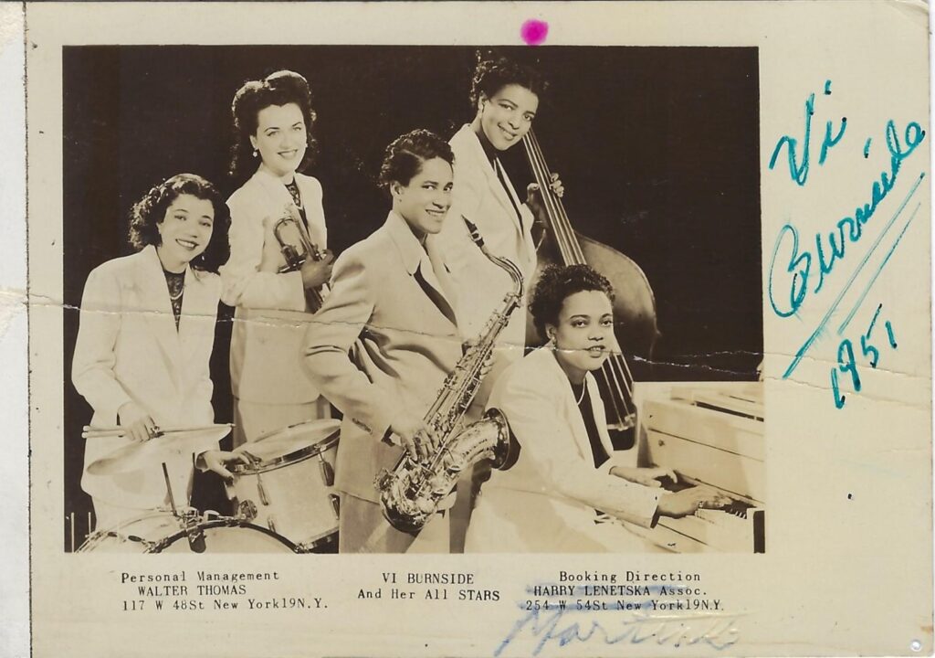 A black and white historic photograph of five women and their various instruments. Vi Burnside is in the center of the photo.