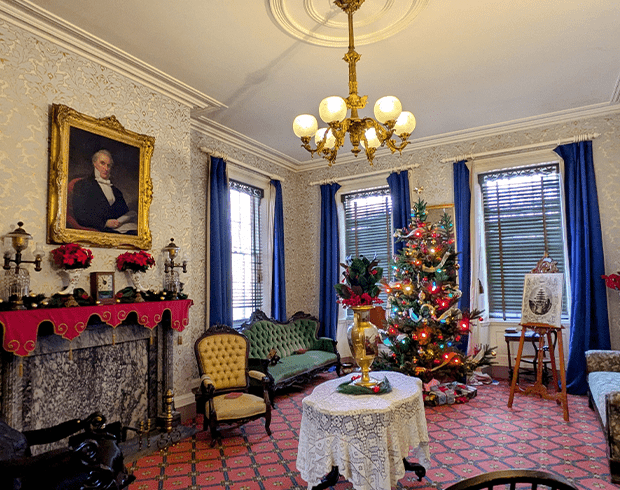 The parlor decorated for Christmas with poinsettias on the mantle and a brightly lit Christmas tree.