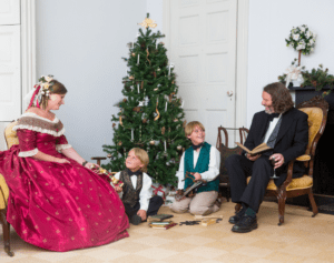 Image of two adults and two children in period costume gathered around a Christmas tree.