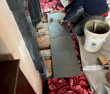 <center><i>Hurst taps the new slate to level it upon the hearth.</center></i> A man taps a large piece of slate into place on the ground, making sure it is level.