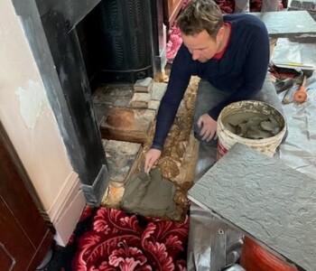 A man applies a layer of mud on the revealed hearth, giving it a sticky foundation on which the slate can be applied.