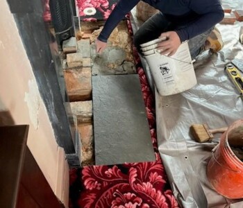 <center><i>Next, the slate, which came in two sections, was laid atop the mud.</center></i> A man applies a layer of mud on top of the stone. The mud will secure the slate top to the ground.