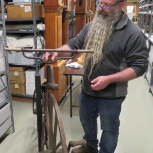 <i> Fabricator Todd Boyer applying the finishing touches by securing the handlebar brace nut. Man standing next to velocipede tightening screw on handlebar riser.