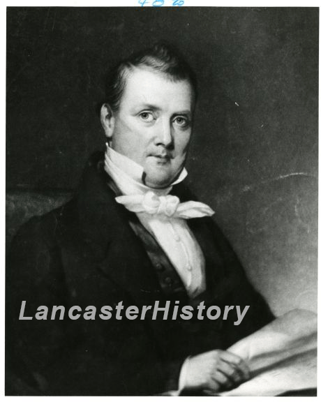 A black and white photograph of a light-skinned man from the chest up. His head is tilted towards the camera. He is wearing a suit with a high collar and neck kerchief. Towards the bottom of the photo, he grips a document in his right hand.